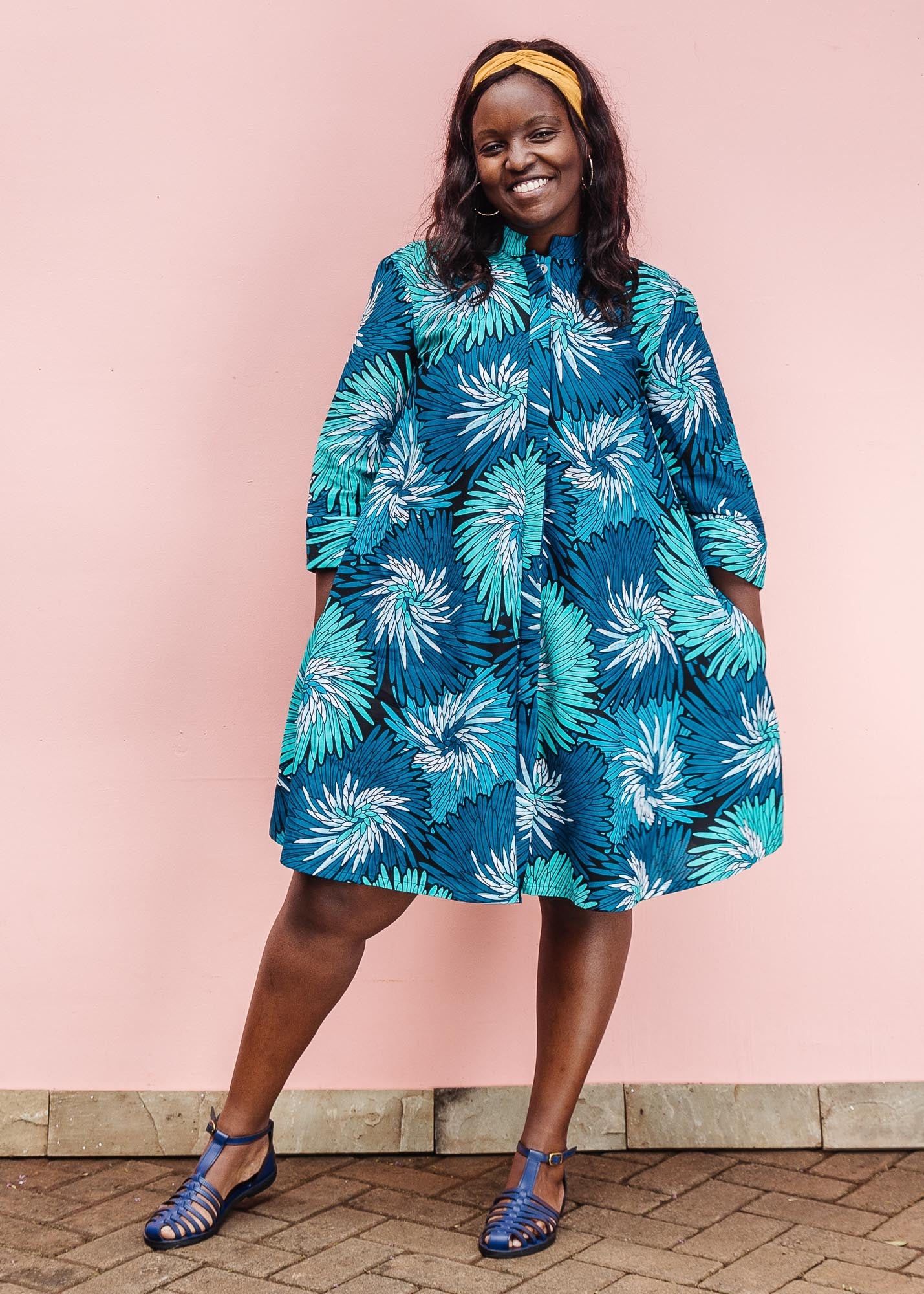 The model is wearing turquoise, black, pacific blue, slate and white feathered spiral print dress