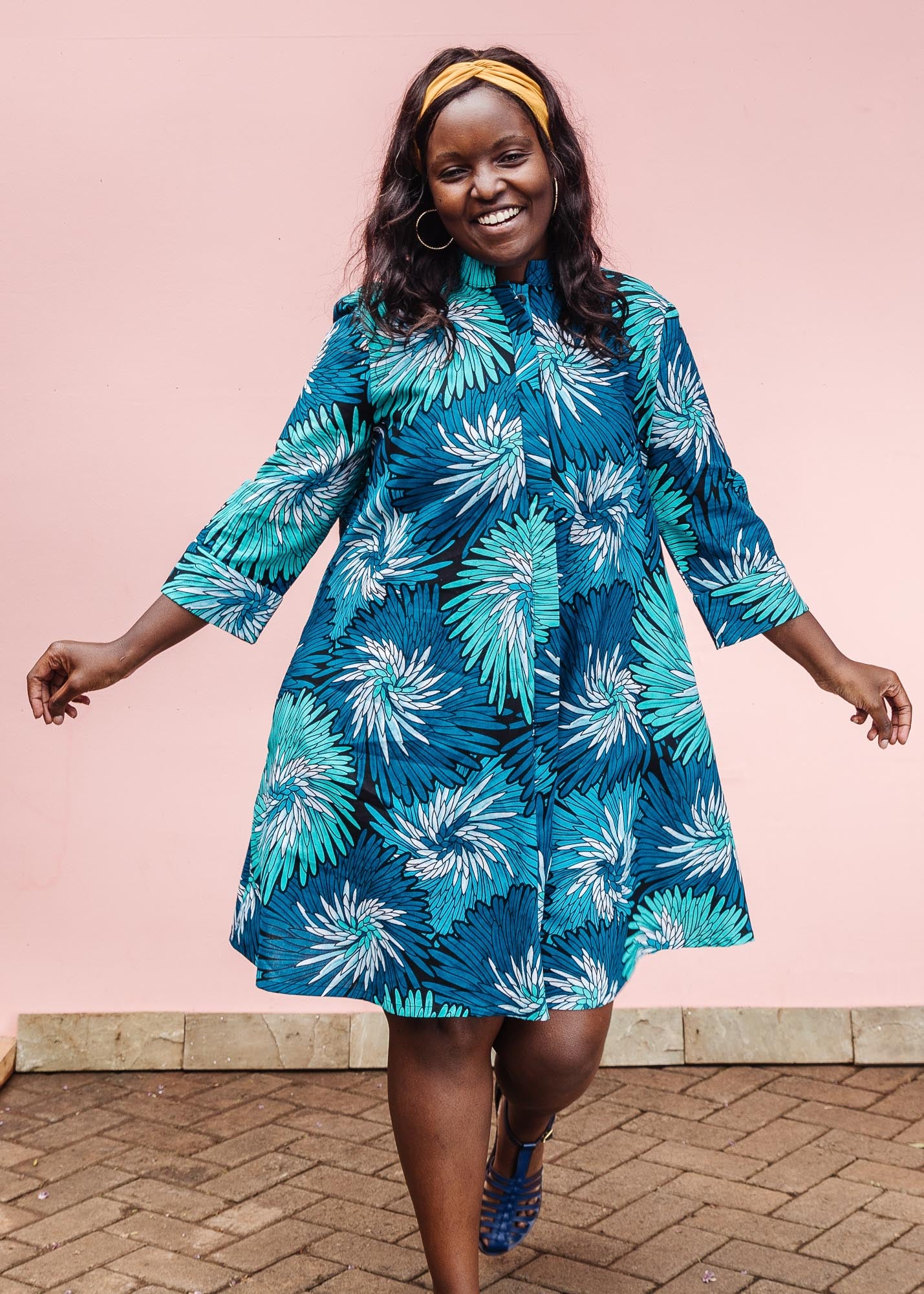 The model is wearing turquoise, black, pacific blue, slate and white feathered spiral print dress