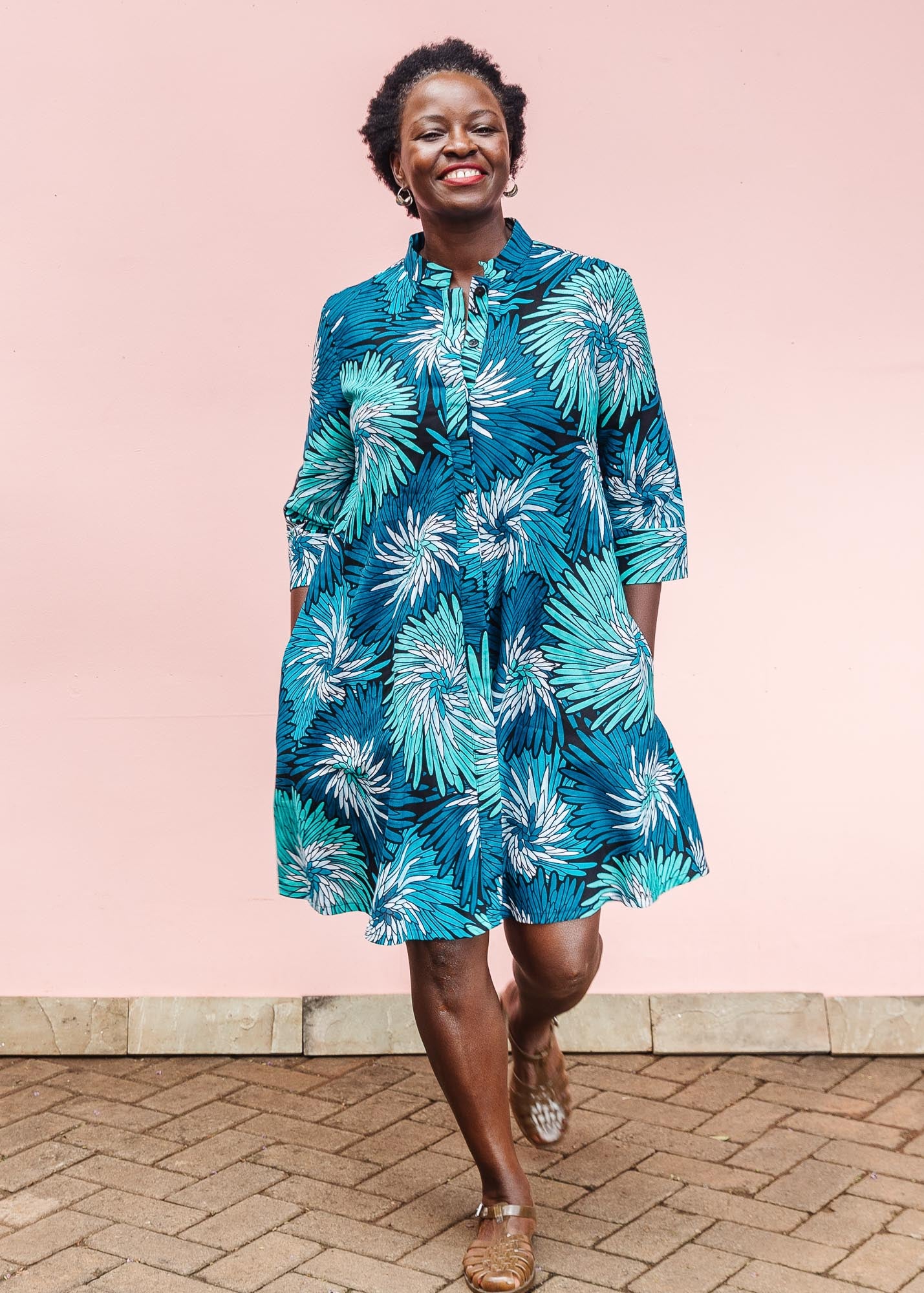 The model is wearing turquoise, black, pacific blue, slate and white feathered spiral print dress
