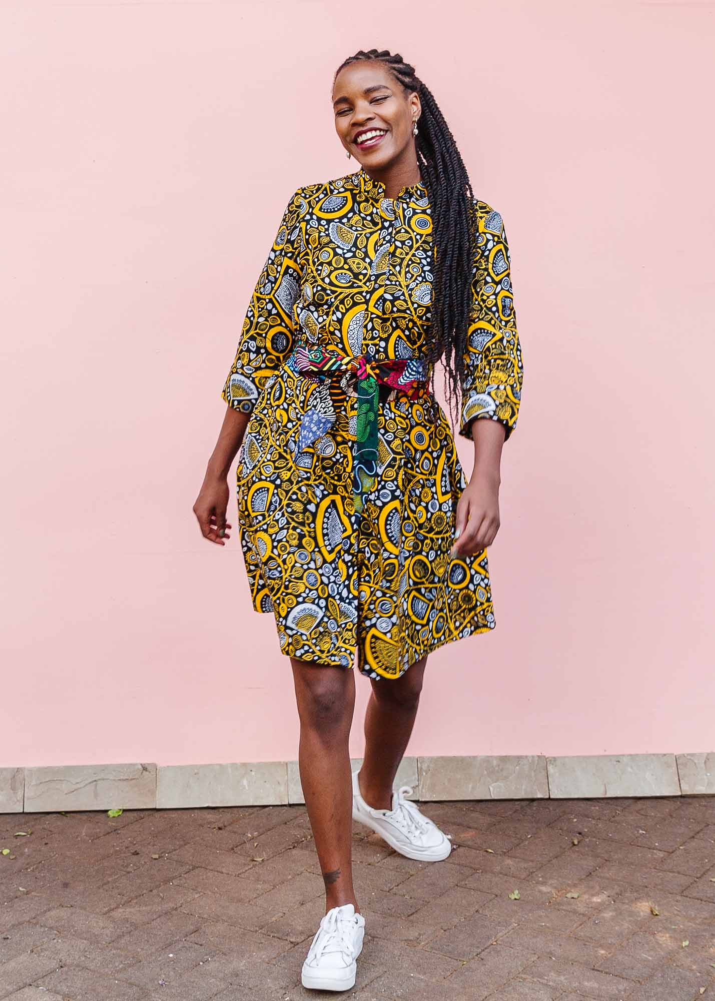 The model is wearing black dress with white and yellow botanical print paired with patchwork belt