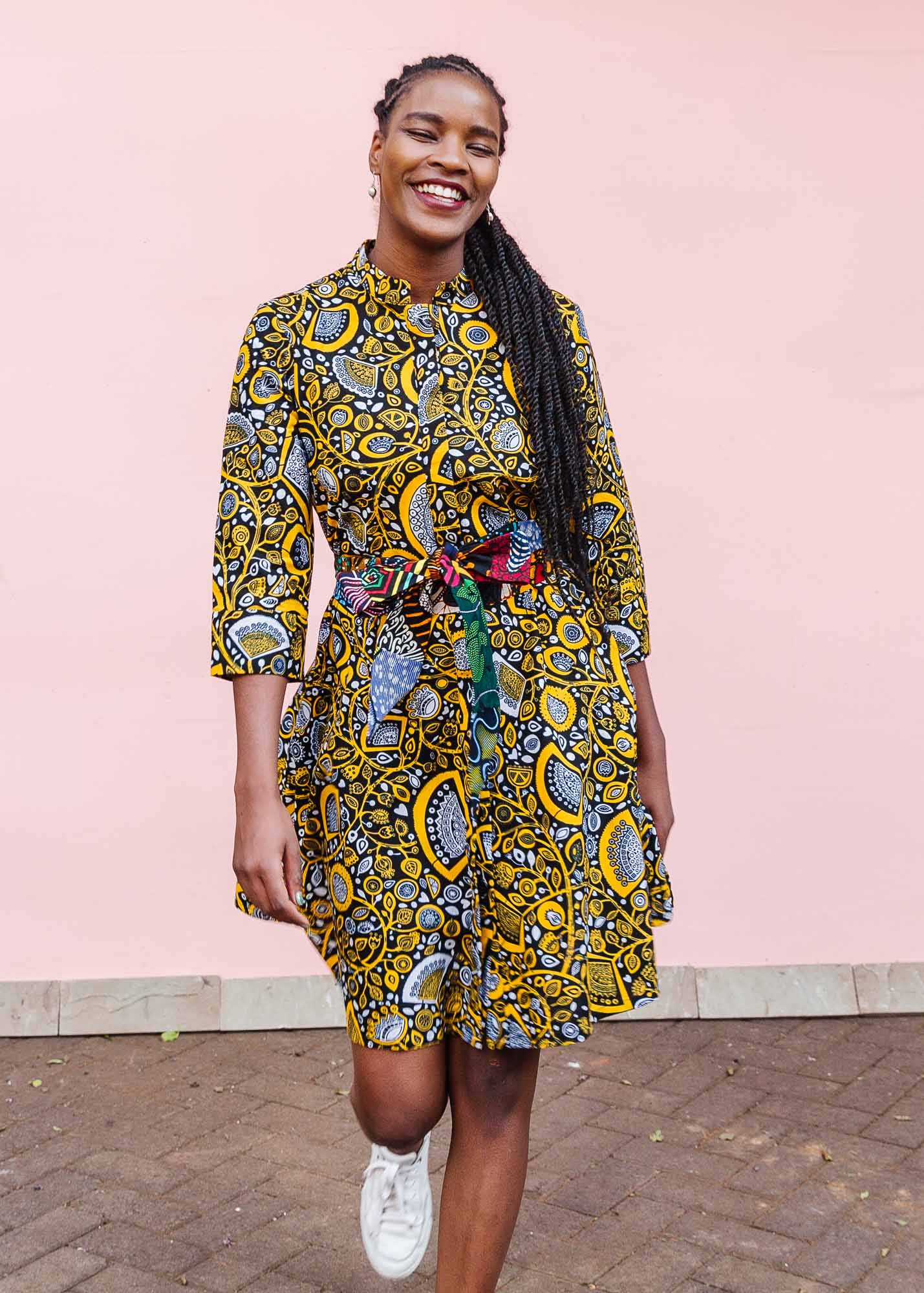 The model is wearing black dress with white and yellow botanical print paired with patchwork belt