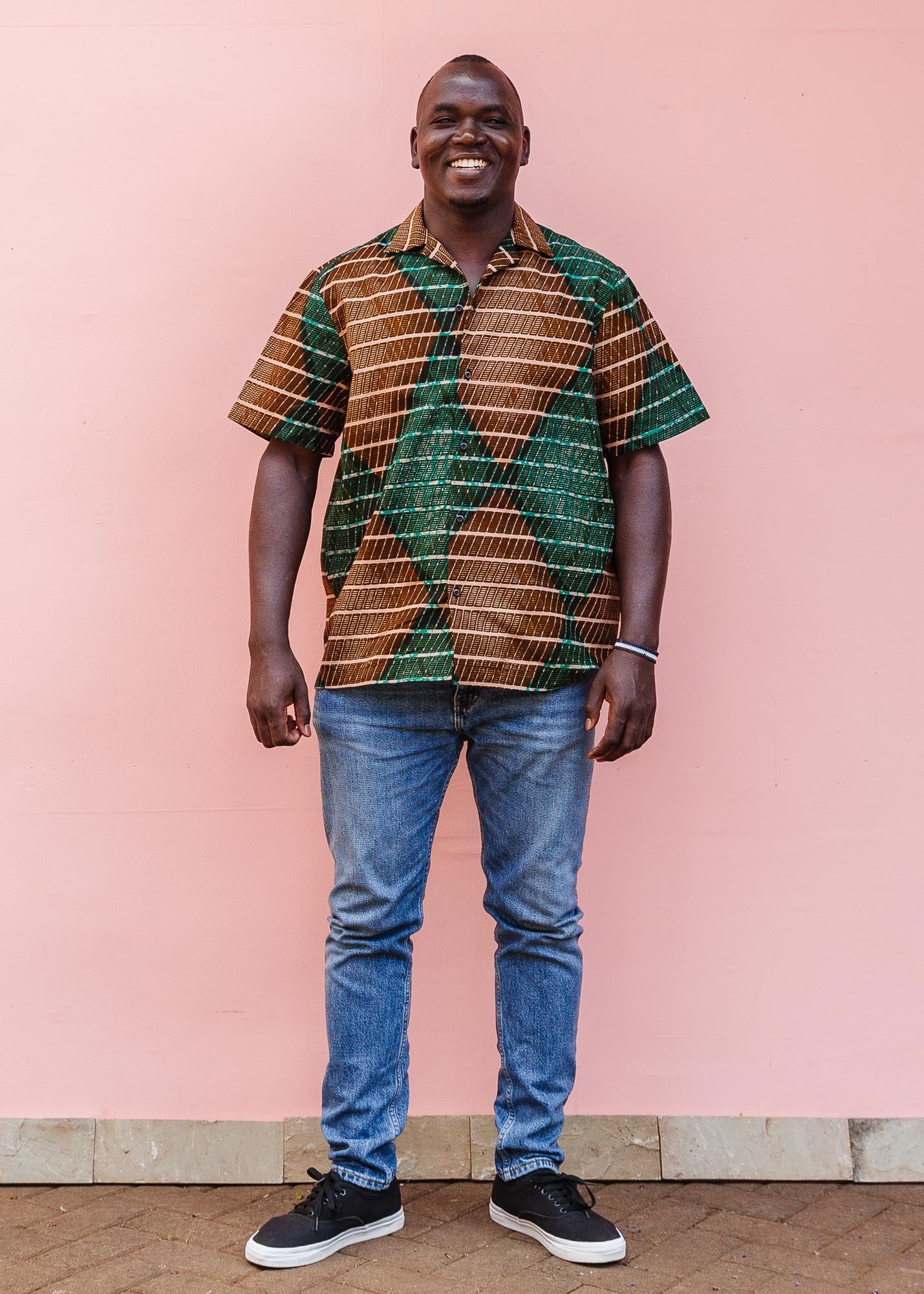 The model is wearing brown, camel, green and black diamond shaped geometric print shirt