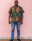 The model is wearing brown, camel, green and black diamond shaped geometric print shirt