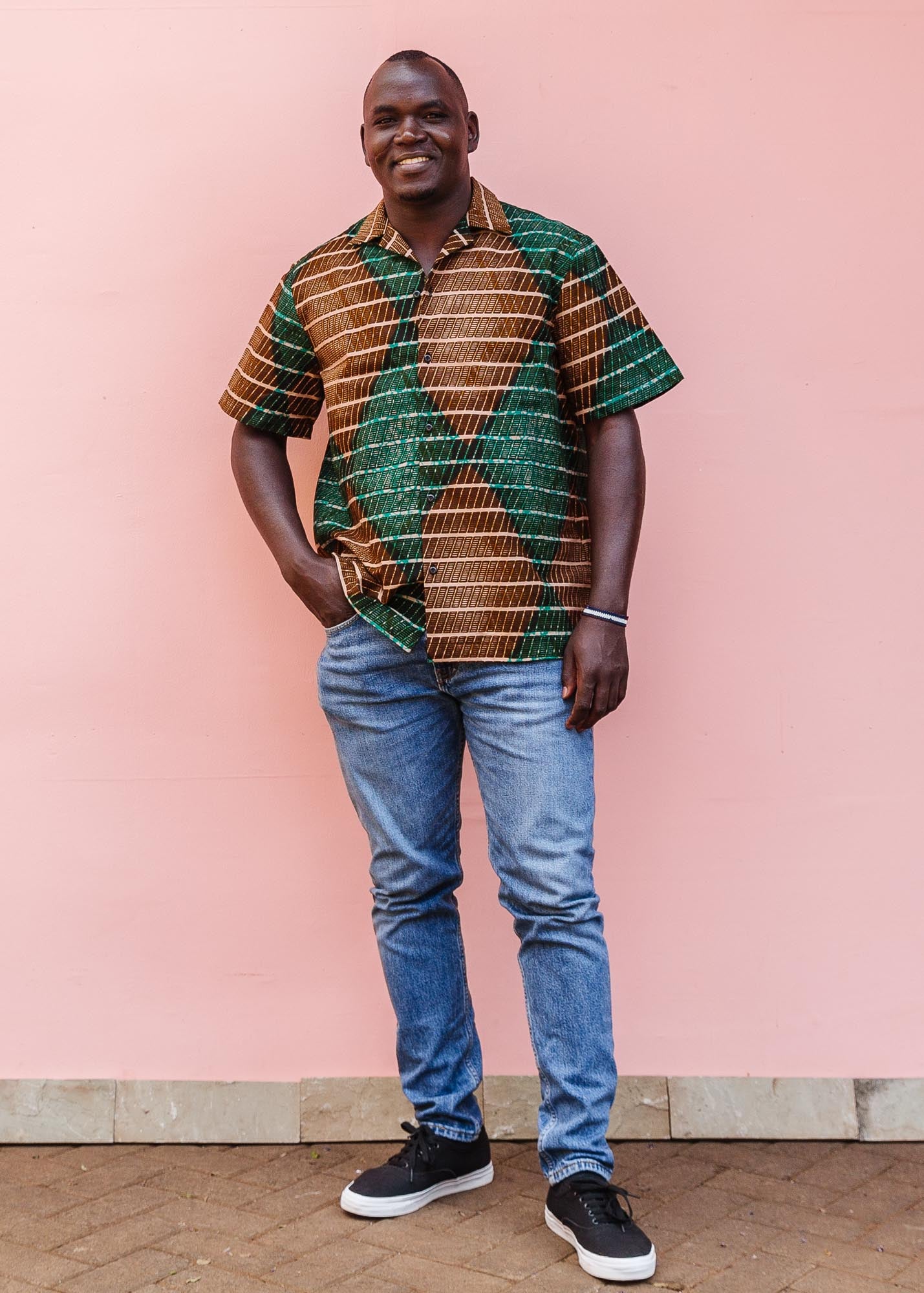 The model is wearing brown, camel, green and black diamond shaped geometric print shirt