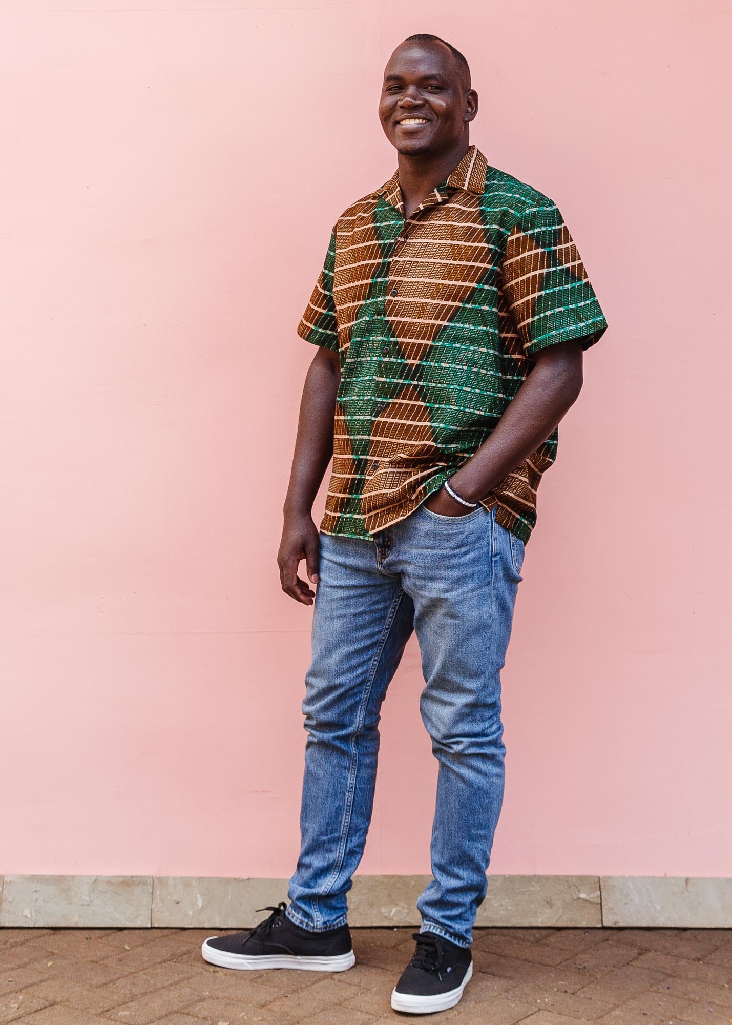 The model is wearing brown, camel, green and black diamond shaped geometric print shirt
