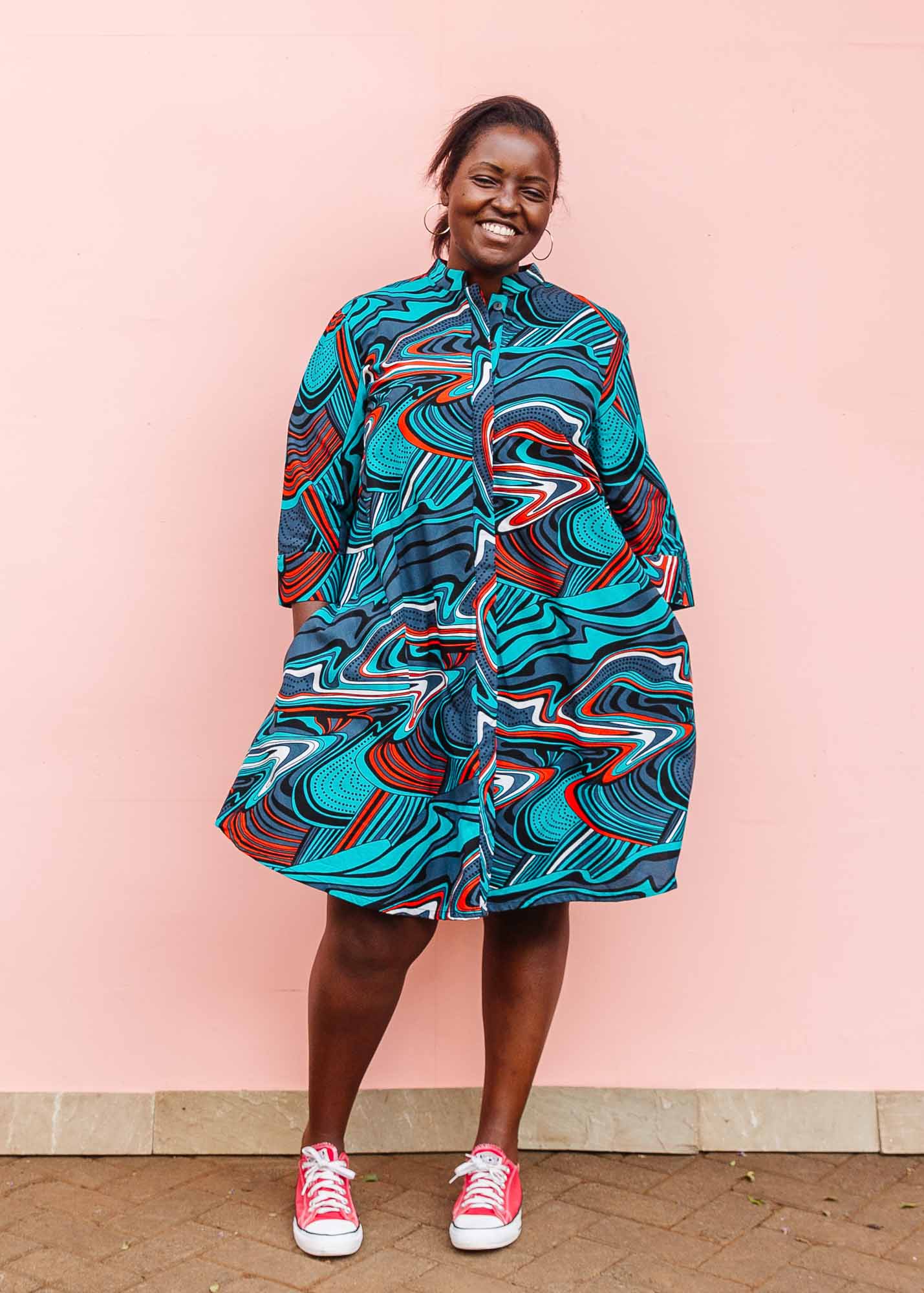 The model is wearing turquoise, black, slate, white and red abstract print dress