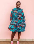 The model is wearing turquoise, black, slate, white and red abstract print dress