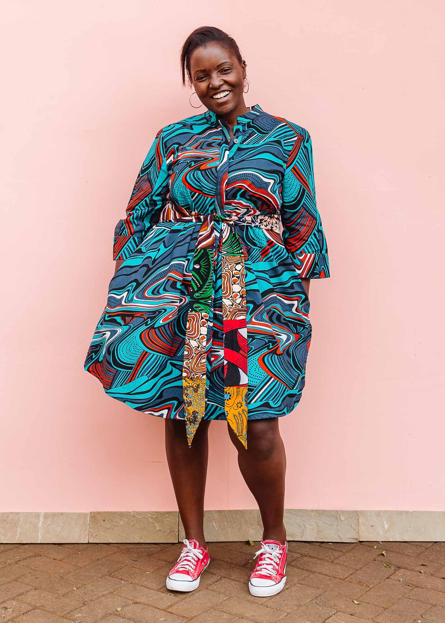 The model is wearing turquoise, black, slate, white and red abstract print dress