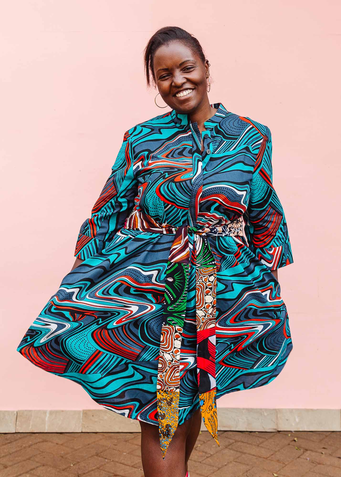 The model is wearing turquoise, black, slate, white and red abstract print dress