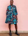 The model is wearing turquoise, black, slate, white and red abstract print dress