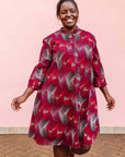 The model is wearing merlot red, brown, red , coral and white abstract line print dress