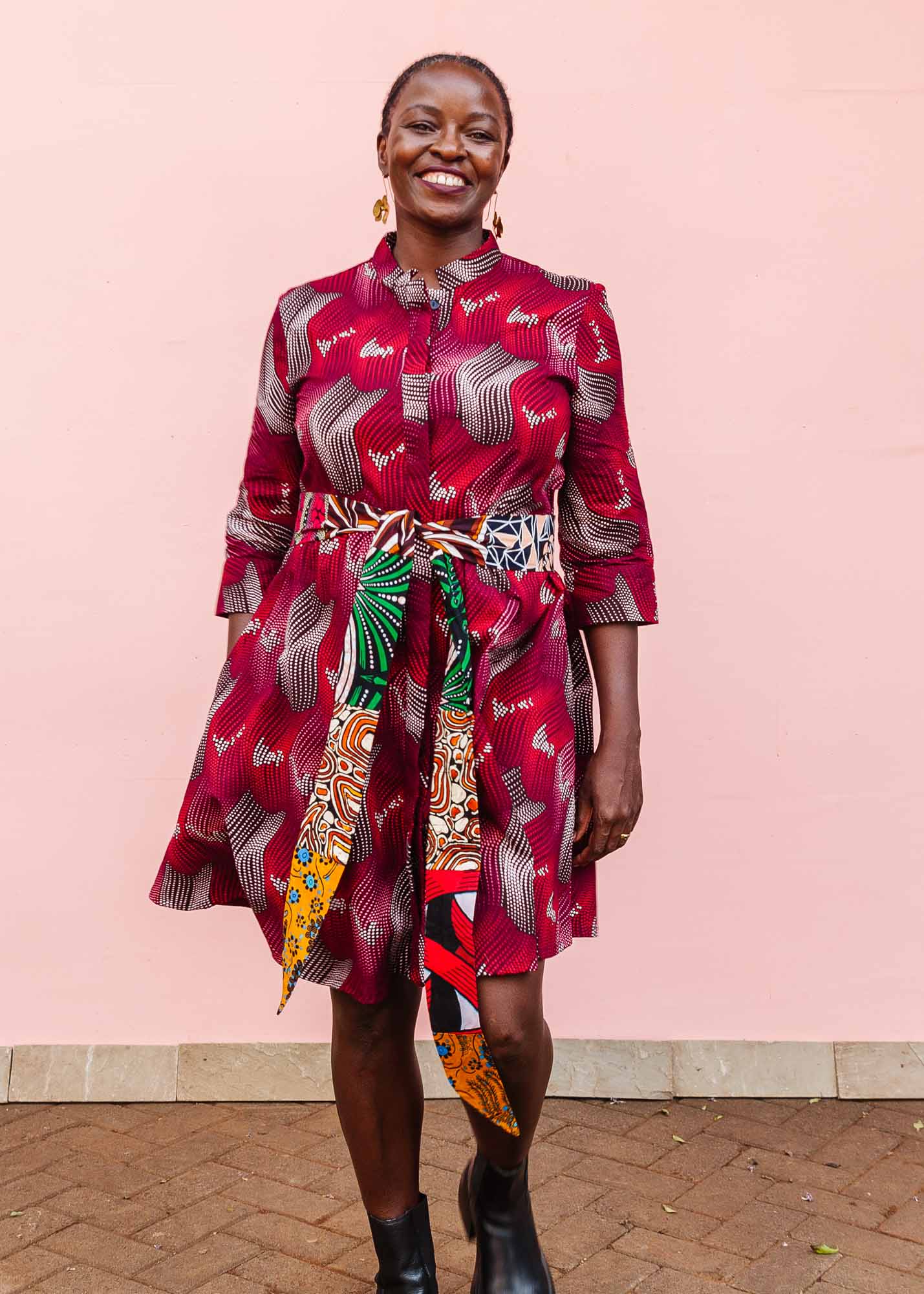 The model is wearing  merlot red, brown, red , coral and white abstract line print dress