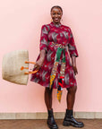 The model is wearing merlot red, brown, red , coral and white abstract line print dress