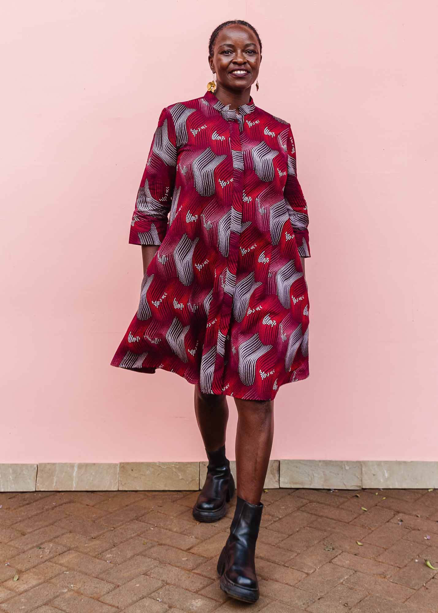 The model is wearing  merlot red, brown, red , coral and white abstract line print dress