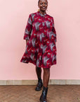 The model is wearing merlot red, brown, red , coral and white abstract line print dress