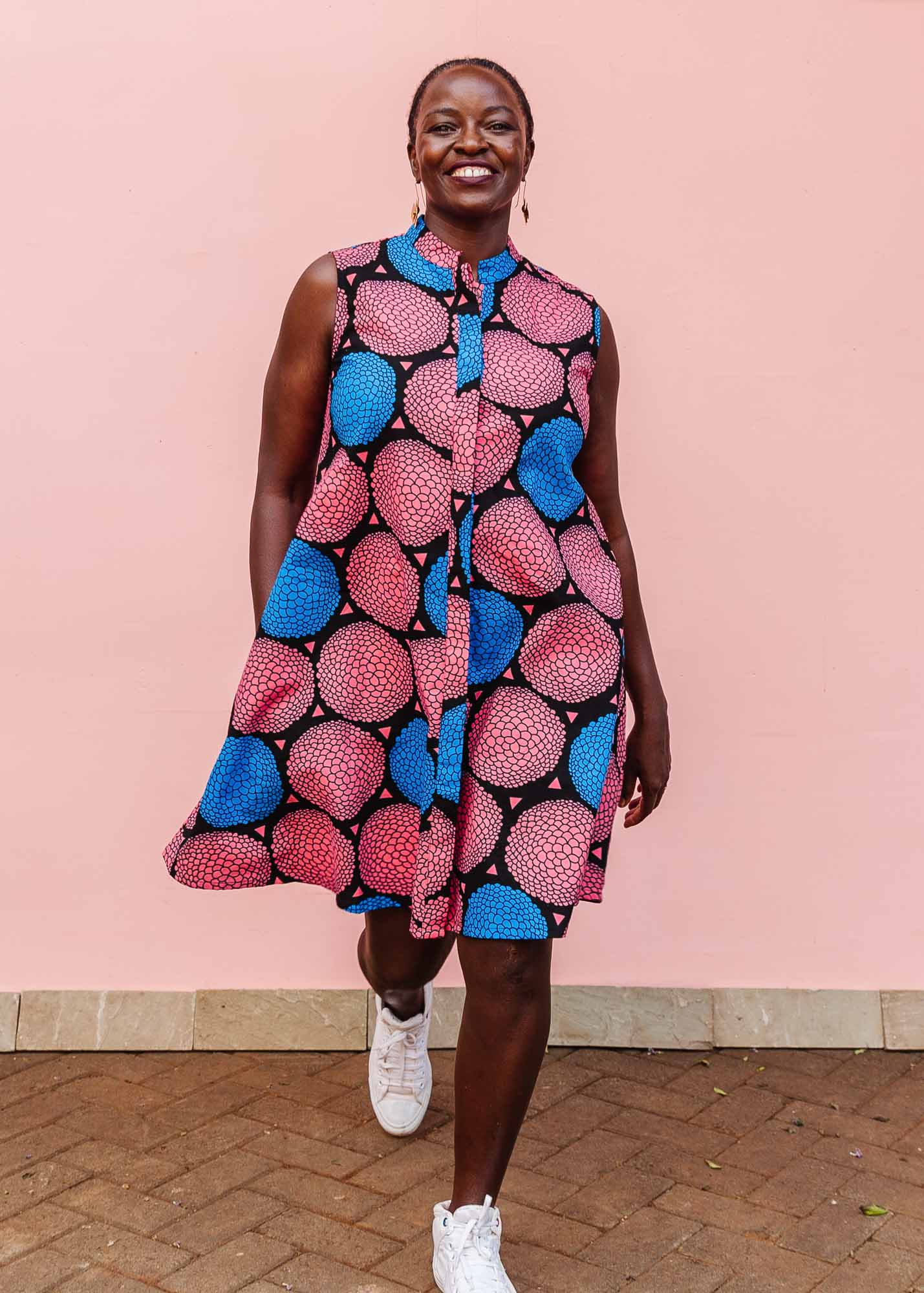 The model is wearing coral, blue and black circular print dress