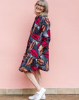 Model wearing a navy dress with red and peach feather print.