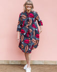 Model wearing a navy dress with red and peach feather print.