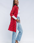 Model wearing red dress with small black and yellow branch design.