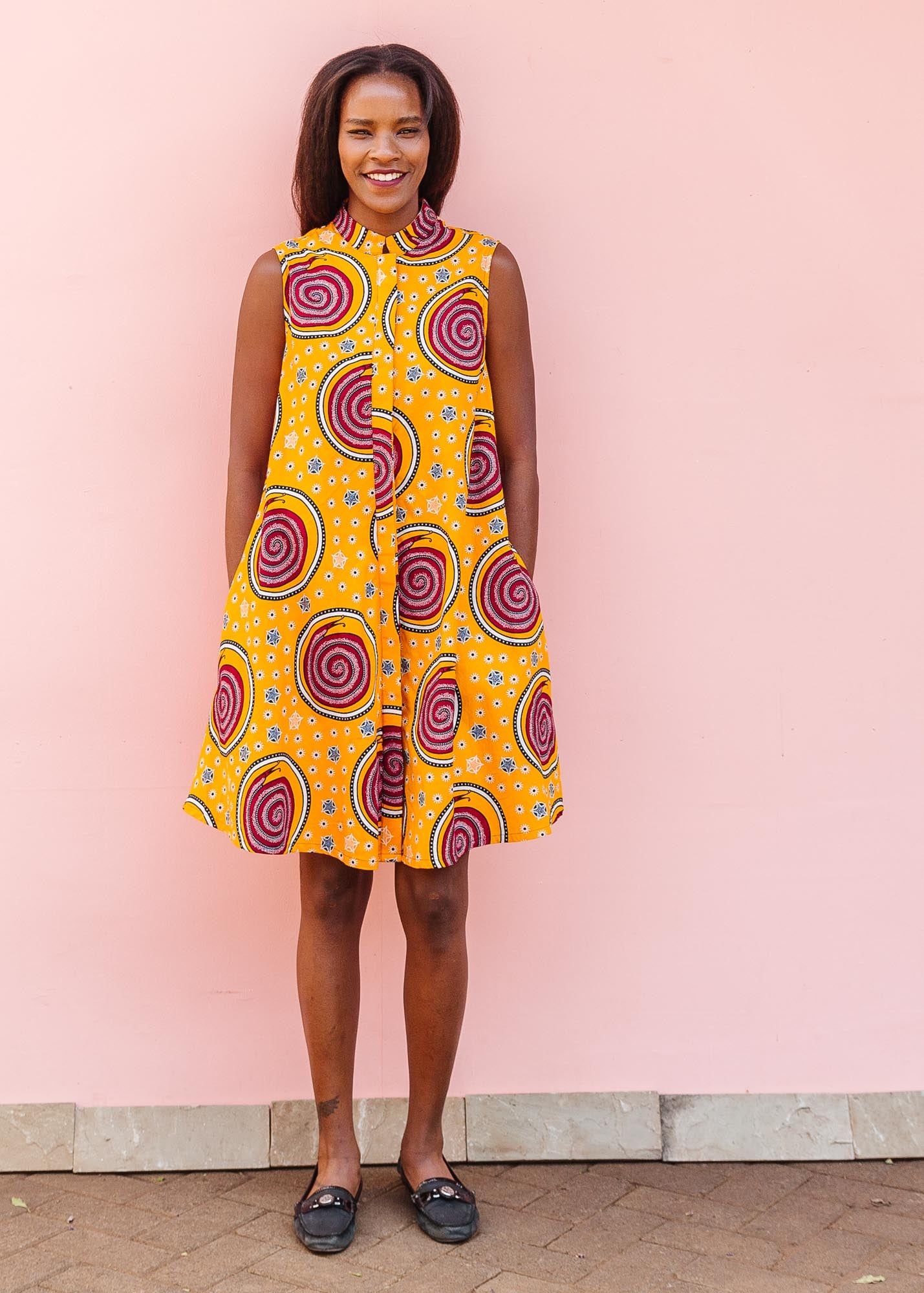 The model is wearing orange white, black and burgundy snail design dress