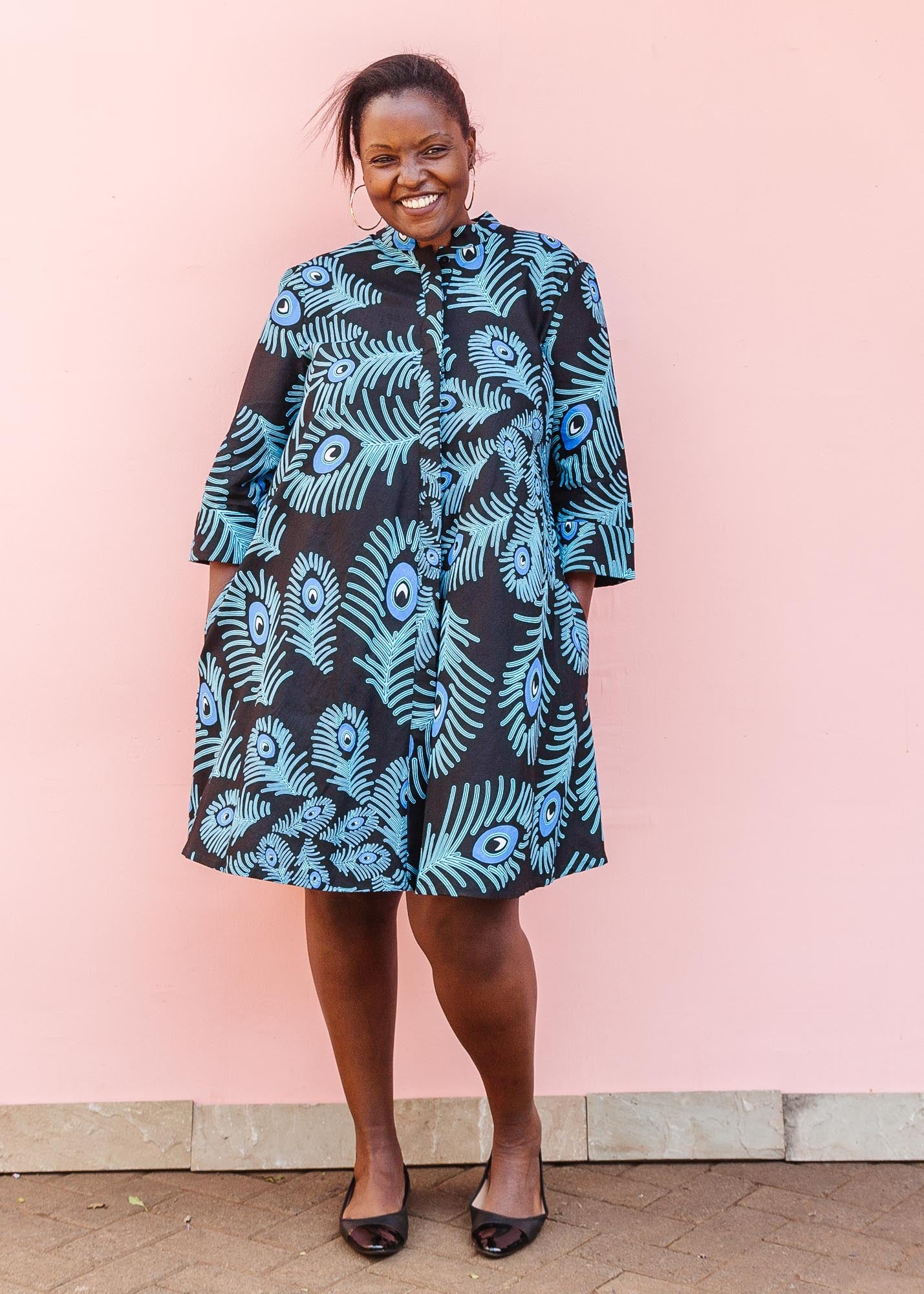 The model is wearing a black dress with blue, white and turquoise peacock feather design print