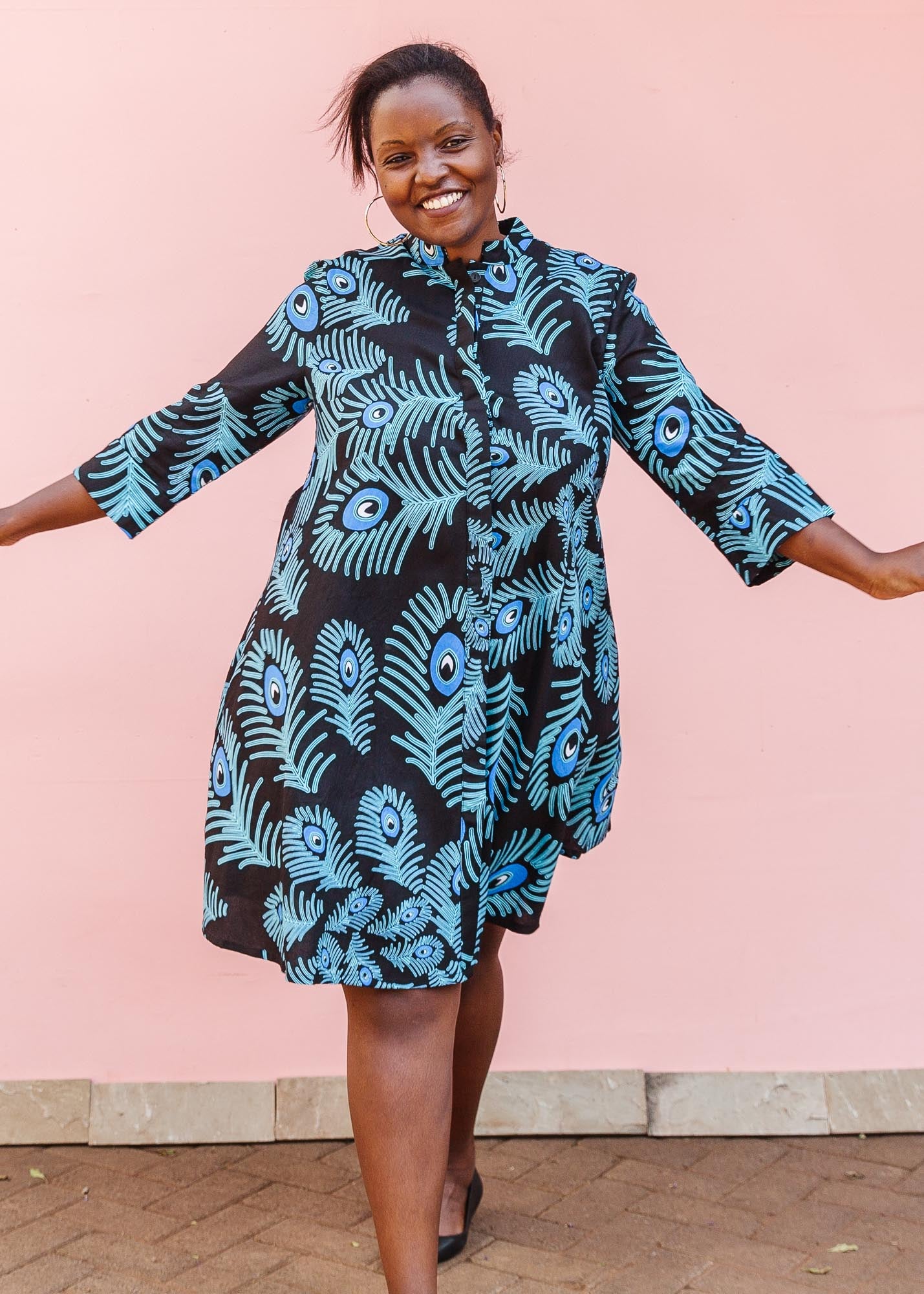The model is wearing a black dress with blue, white and turquoise peacock feather design print