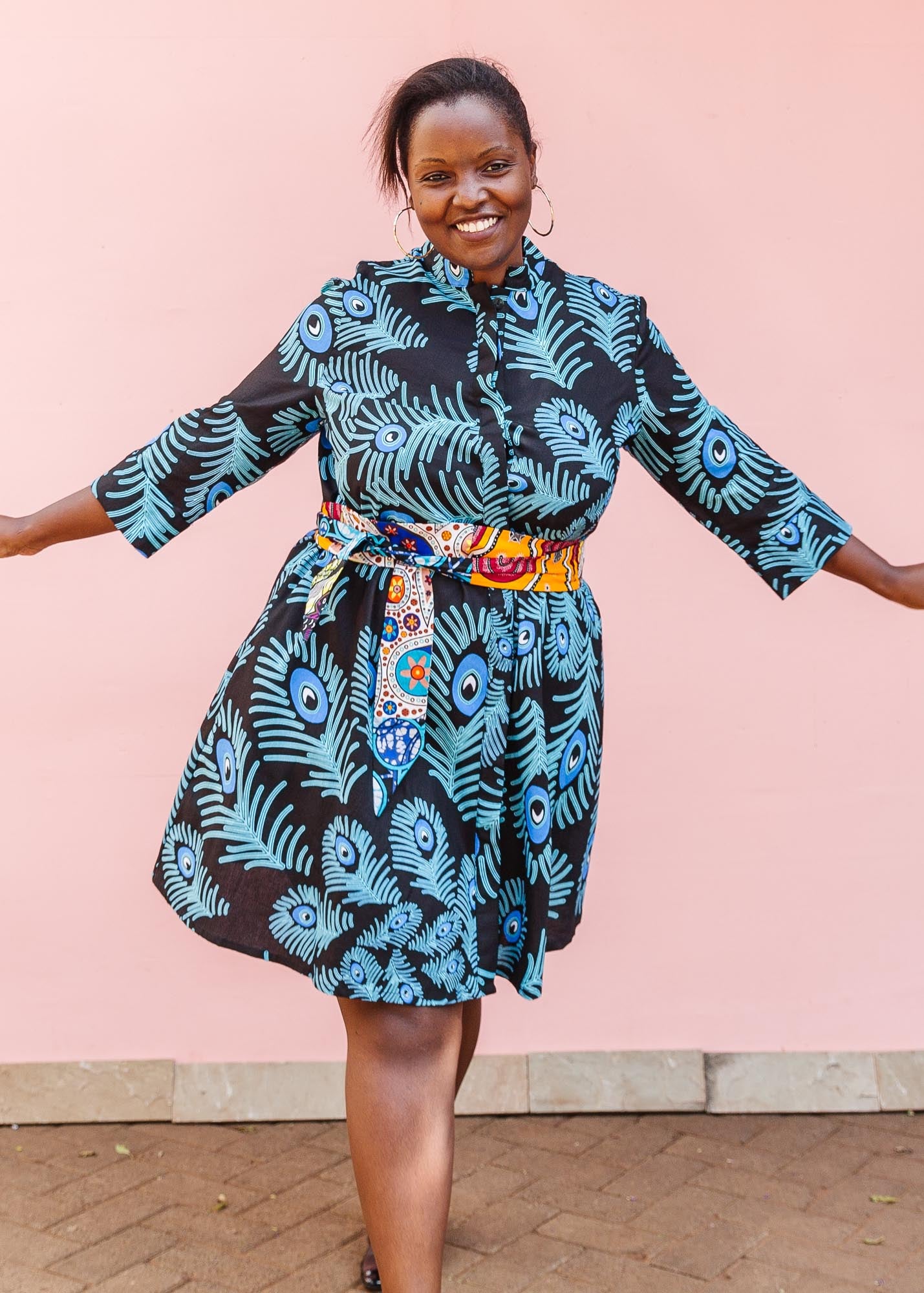 The model is wearing a black dress with blue, white and turquoise peacock feather design print   