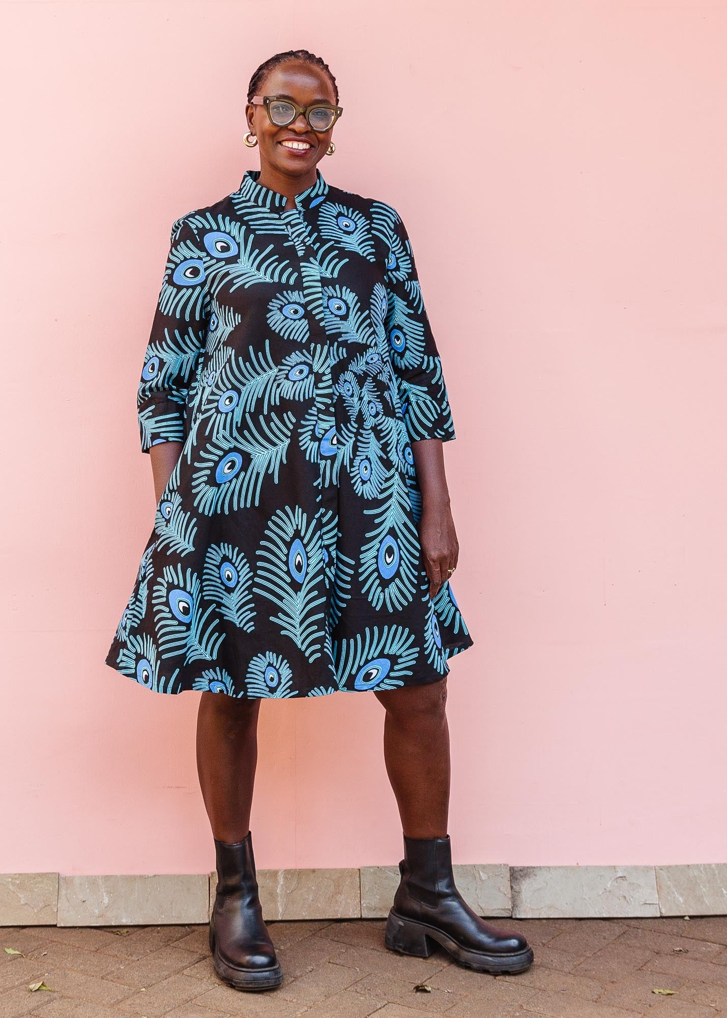 The model is wearing a black dress with blue, white and turquoise peacock feather design print