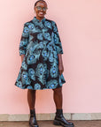 The model is wearing a black dress with blue, white and turquoise peacock feather design print