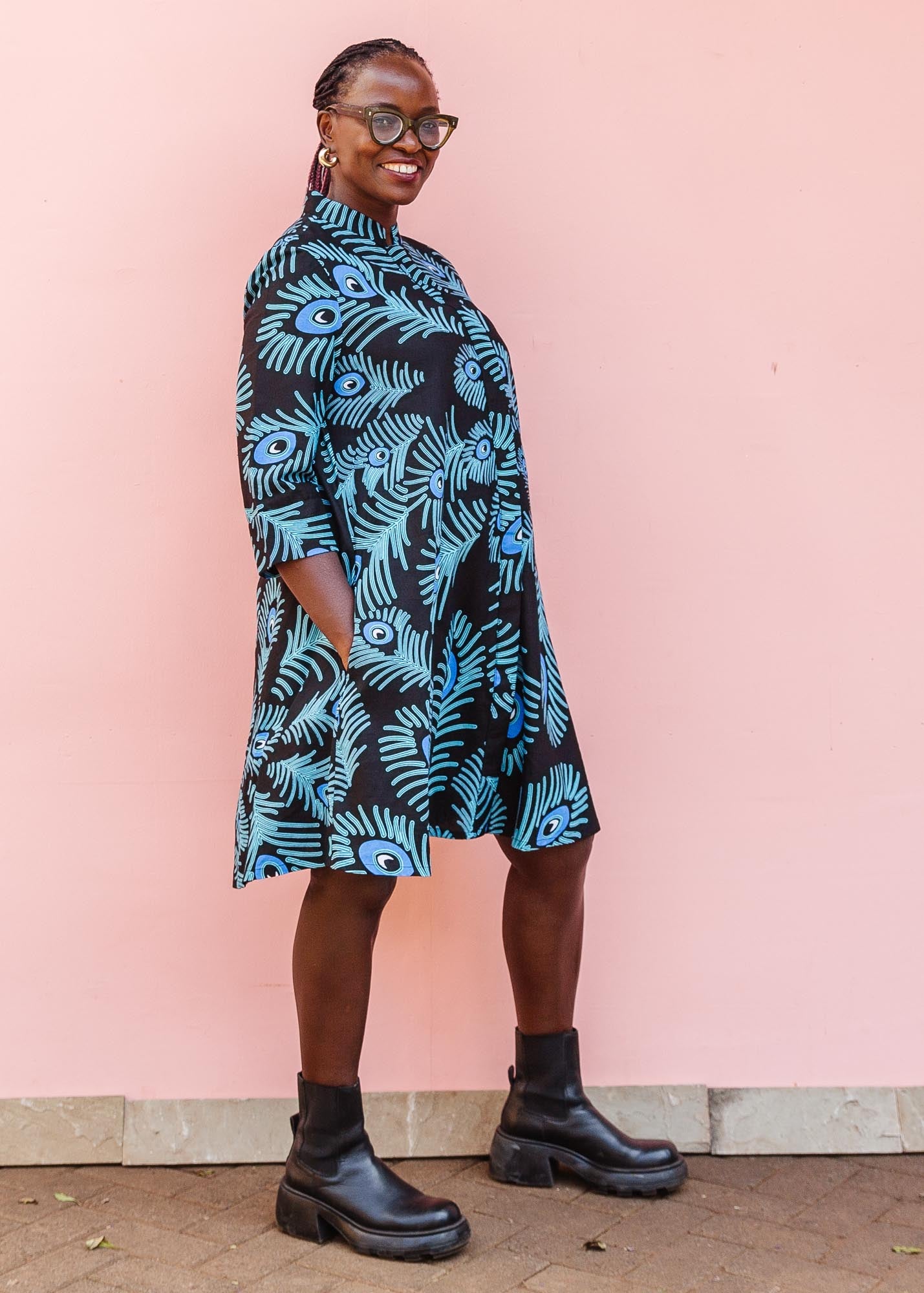 The model is wearing a black dress with blue, white and turquoise peacock feather design print