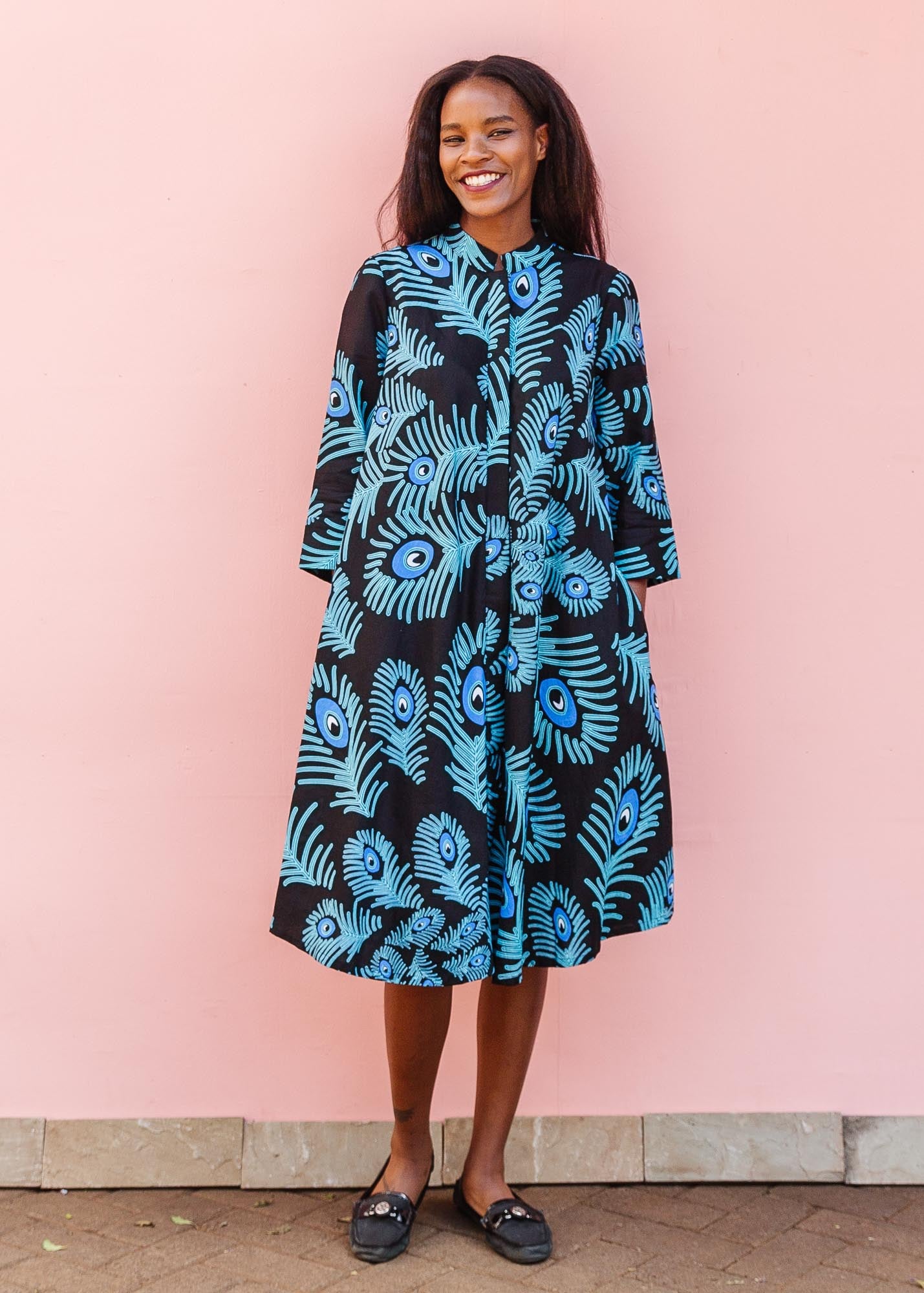 The model is wearing a black dress with blue, white and turquoise peacock feather design print