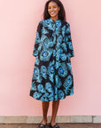 The model is wearing a black dress with blue, white and turquoise peacock feather design print