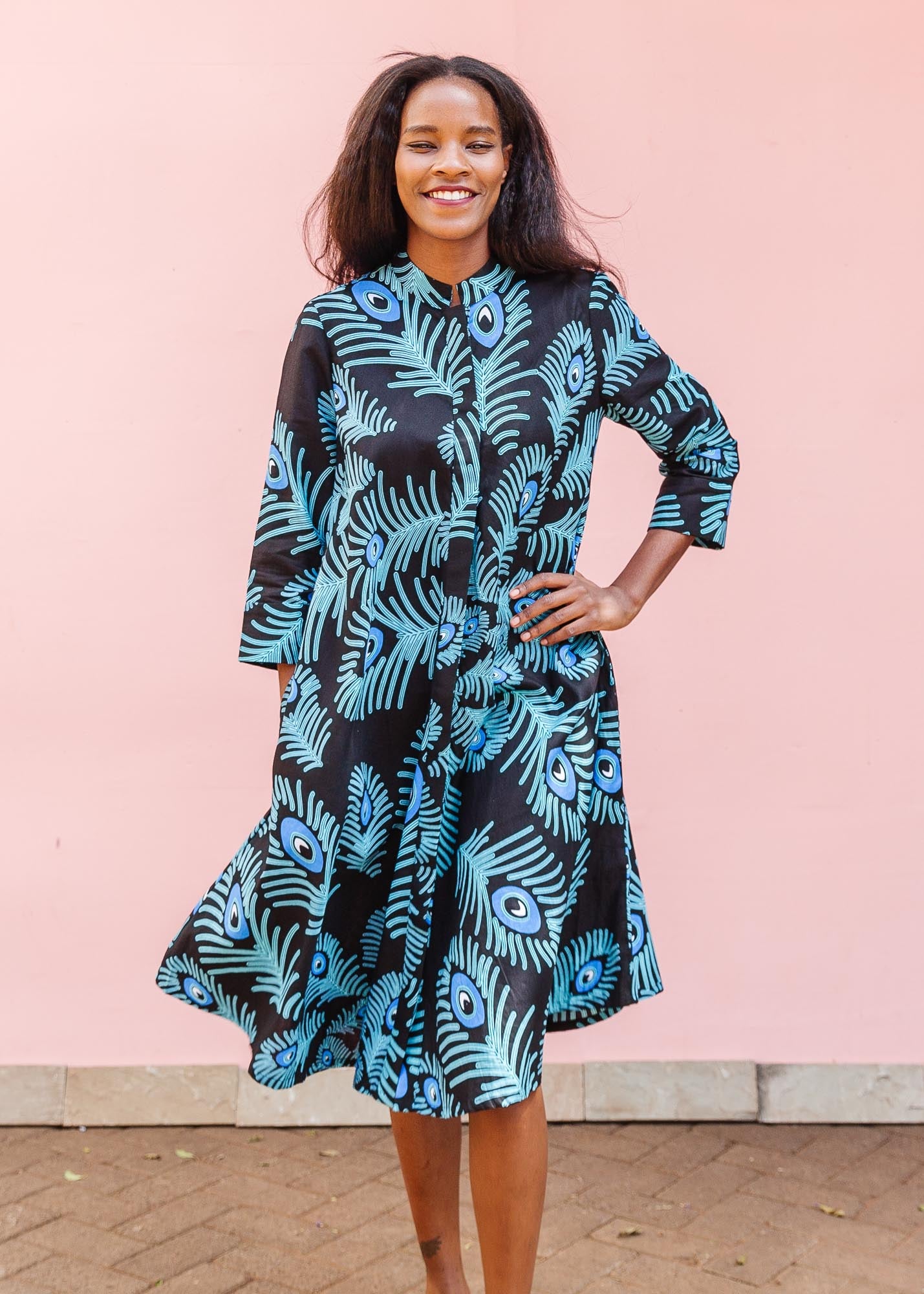 The model is wearing a black dress with blue, white and turquoise peacock feather design print