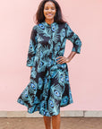 The model is wearing a black dress with blue, white and turquoise peacock feather design print