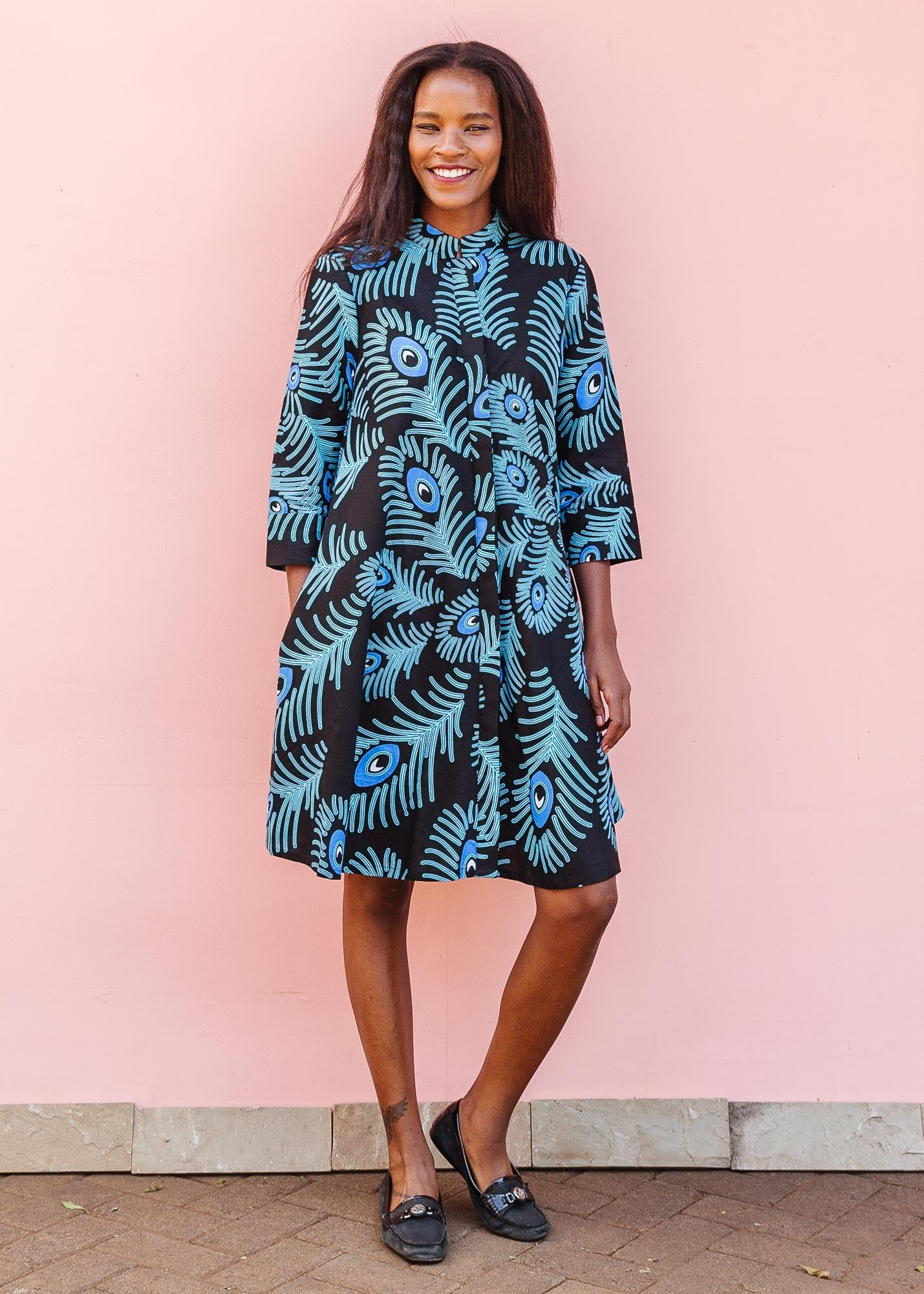 The model is wearing a black dress with blue, white and turquoise peacock feather design print