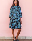 The model is wearing a black dress with blue, white and turquoise peacock feather design print