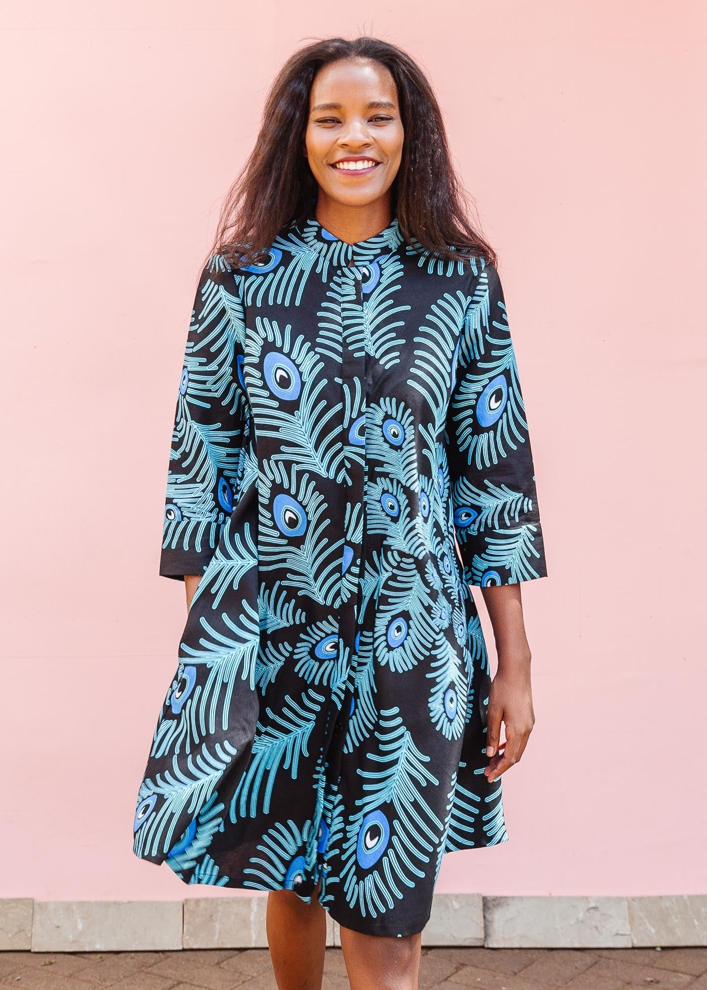 The model is wearing a black dress with blue, white and turquoise peacock feather design print