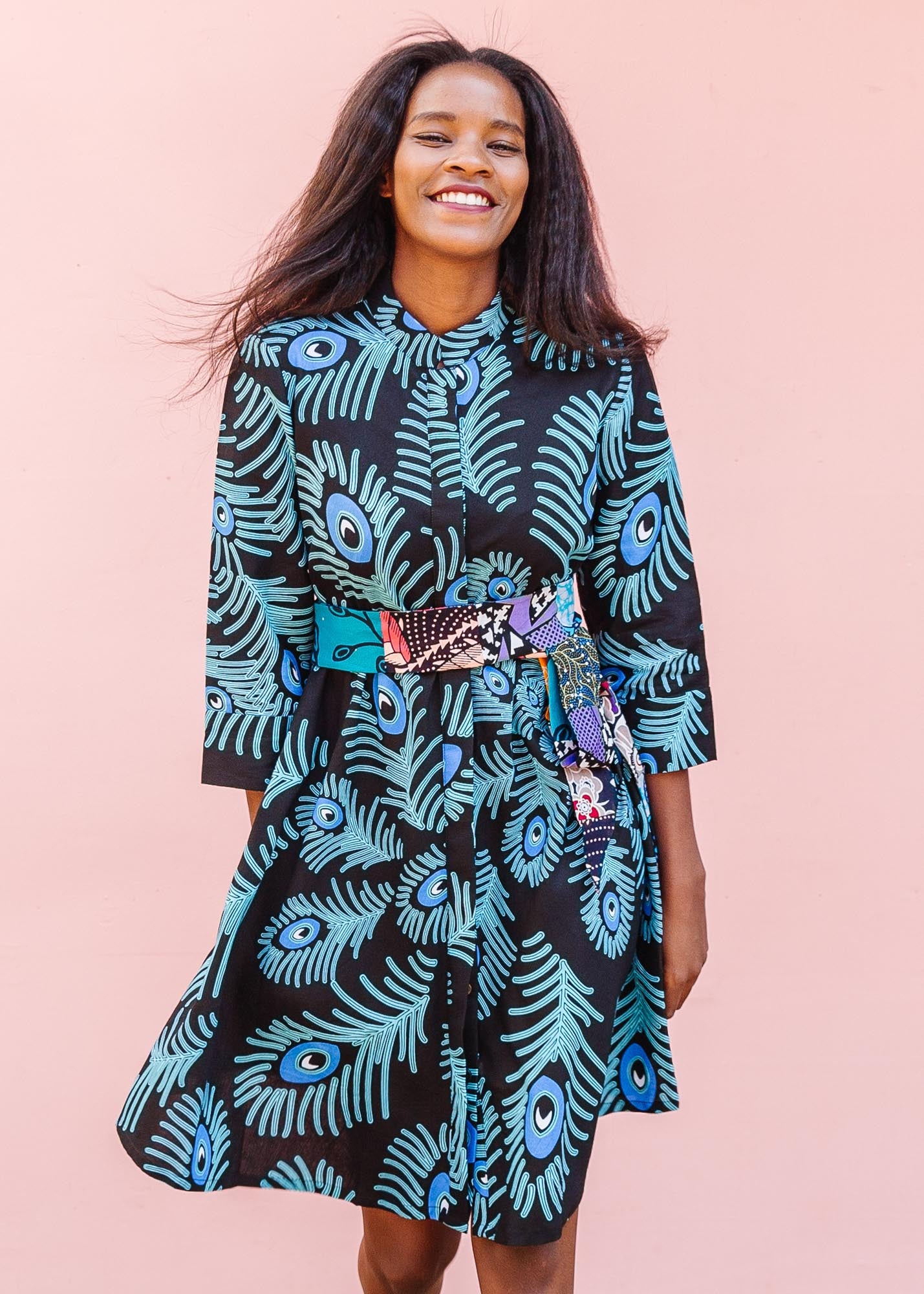 The model is wearing a black dress with blue, white and turquoise peacock feather design print