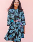 The model is wearing a black dress with blue, white and turquoise peacock feather design print