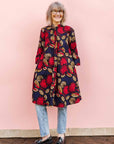 The model is wearing navy dress with red, white and orange floral print
