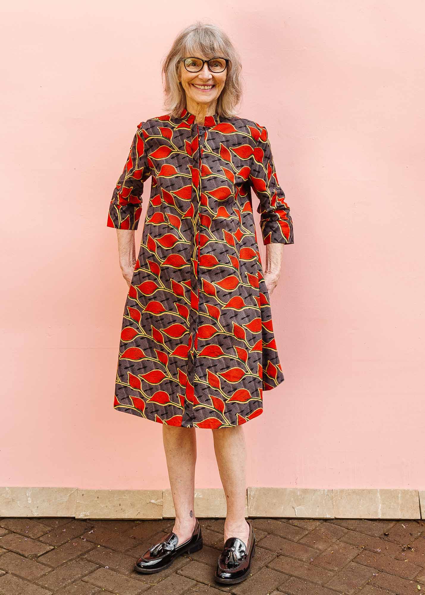 The model is wearing grey dress with red, yellow and black leaf print