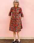 The model is wearing grey dress with red, yellow and black leaf print