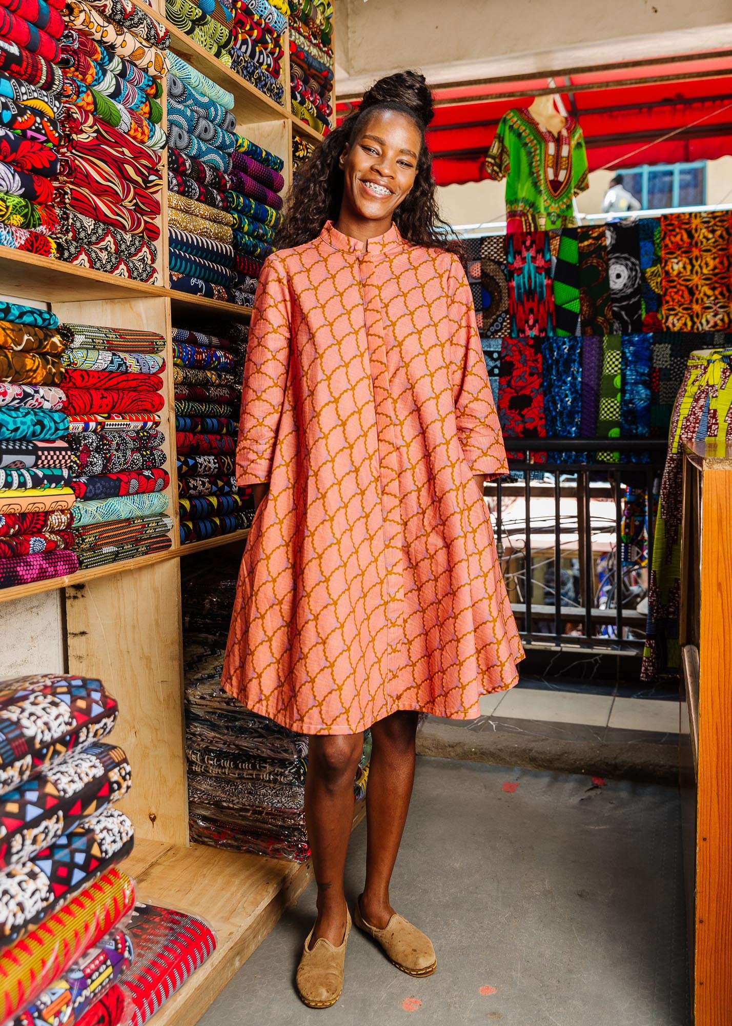 The model is wearing peach-pink, lavender and brown seashell print dress