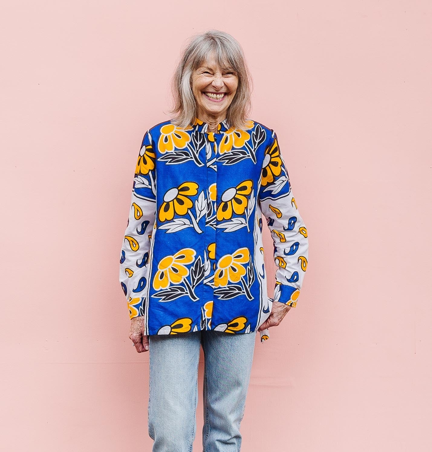 The model is wearing white, blue, black and orange mixed pattern long sleeved kanga shirt