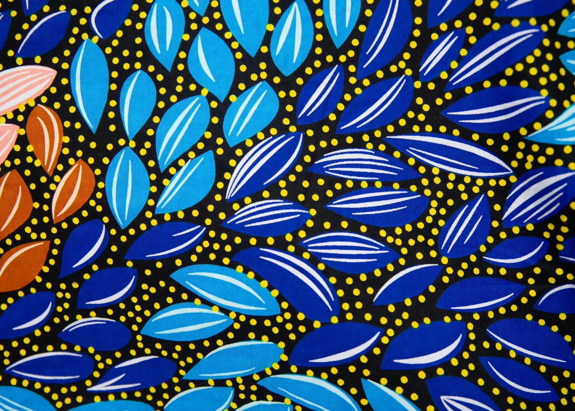 Close up display of black dress with yellow dots and brown, blues, peach leaves.