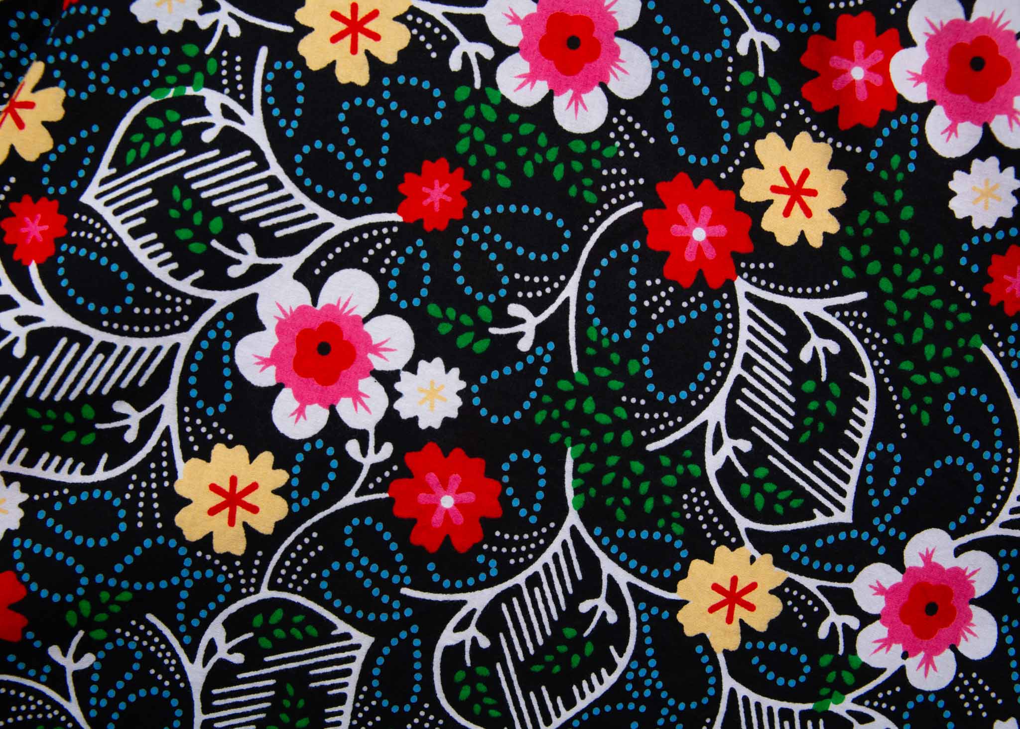 Close up display of black dress with white, green, red and yellow floral print, fabric.
