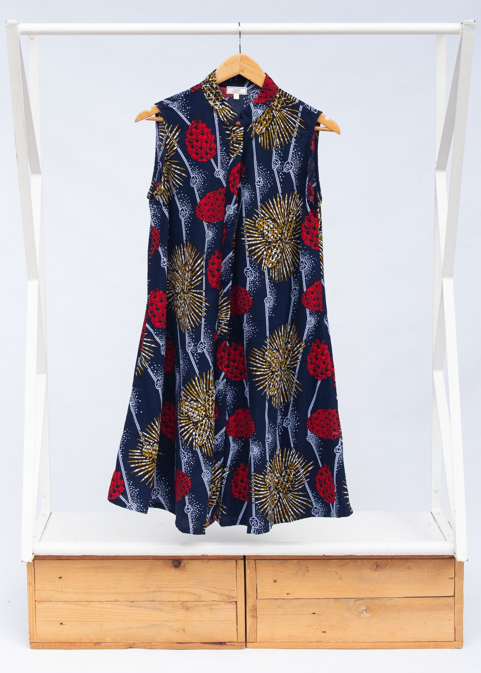 Display of navy sleeveless dress with red, yellow and white splatter print.