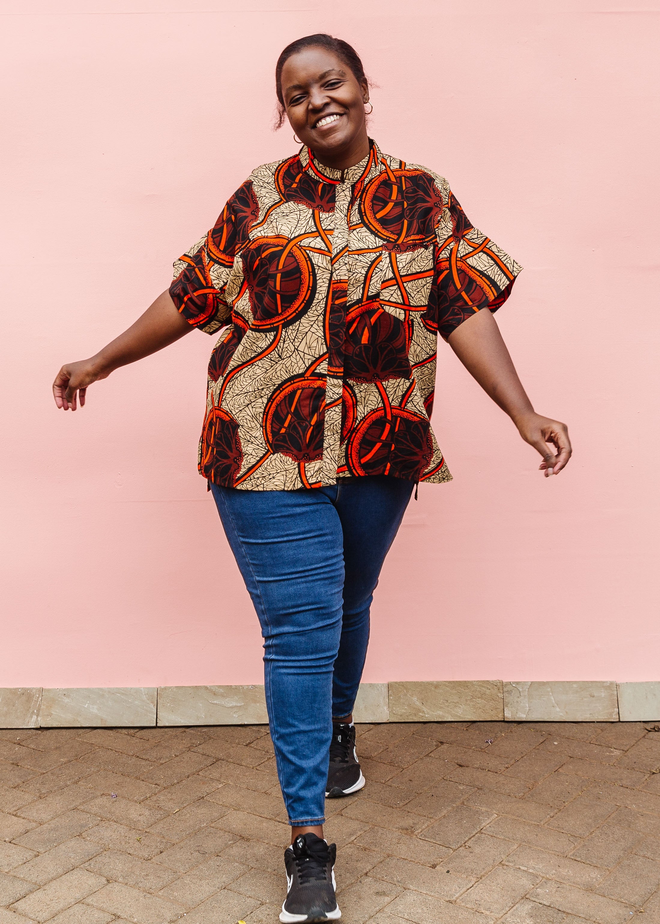 Model wearing beige shirt with brown and orange circles and lines.