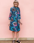 Model wearing black dress with colorful peacock print.