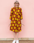 Model wearing red dress with yellow and brown flowers.